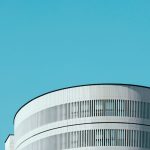 Minimalist architectural design with a focus on a cylindrical building under a clear blue sky.