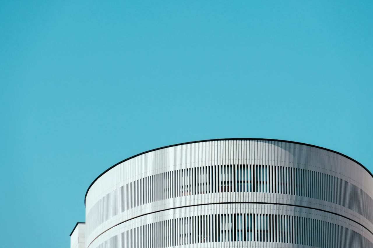 Minimalist architectural design with a focus on a cylindrical building under a clear blue sky.